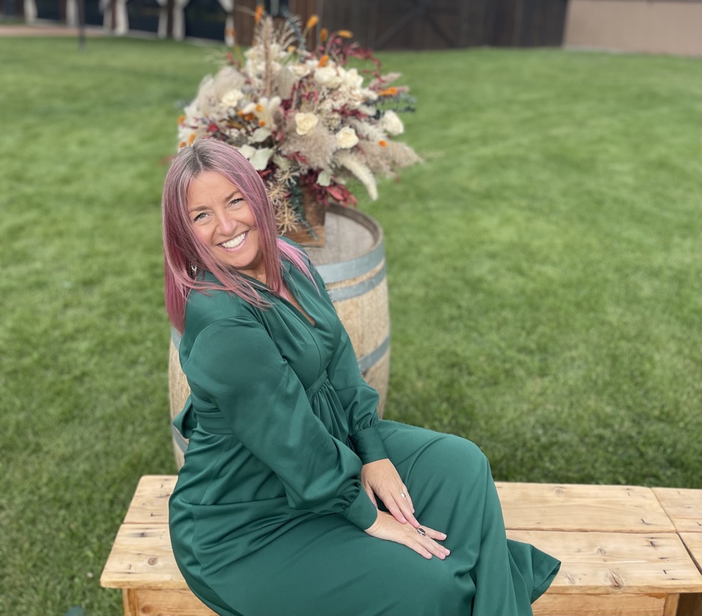 Portrait photo of Michelle Mejaski with long pink hair, smiling outside.